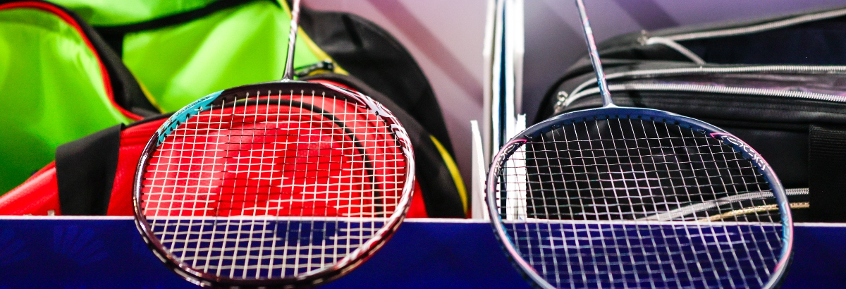 Two badminton rackets lying on kit boxes at the side of a court